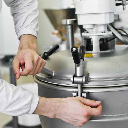 Photograph showing a worker's hands tightning down the lid of an industrial food mixer.