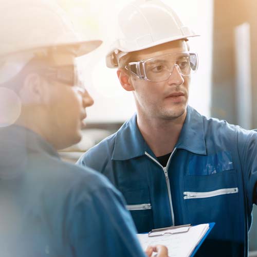 A factory manager and direct report review a checklist for operations.