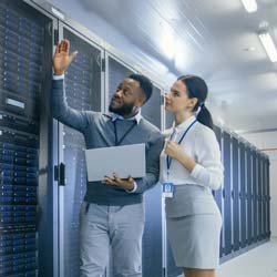 A professional looking man and woman stand in front of a data center's server array.